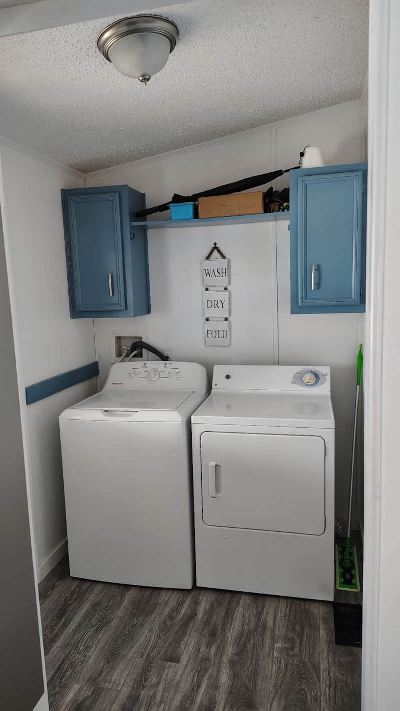 Dedicated laundry room with side-by-side washer and dryer, wood-look flooring, and blue upper cabinets at Lichner Resort Stays