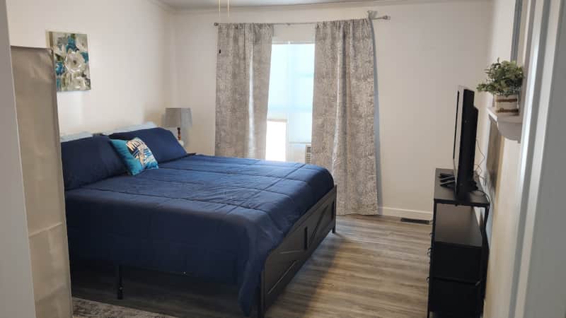 Primary King Suite bedroom with navy bedding, floating shelf, flat-screen TV, and wood-look flooring at Lichner Resort Stays