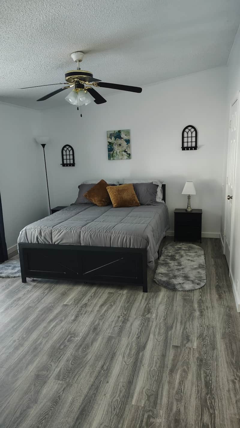 Queen Guest Room with black wood-frame queen bed, gray quilted bedding, mustard accent pillows, matching black nightstands, and modern farmhouse decor at Lichner Resort Stays